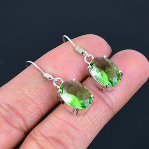 May include: A pair of silver dangle earrings with oval-shaped green gemstones.