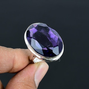 May include: A silver ring with a large, oval-shaped amethyst gemstone. The gemstone is faceted and has a deep purple color.