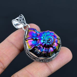 Peut inclure: Un pendentif en argent avec un fossile d'ammonite iridescent aux couleurs de l'arc-en-ciel. Le pendentif est serti dans un cadre en argent aux détails complexes.