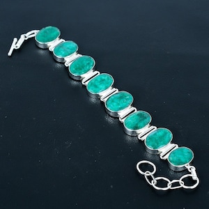 Può includere: Un bracciale in argento con pietre preziose ovali di colore verde brillante. Ogni pietra è incastonata in una lunetta d'argento e collegata da maglie. Il bracciale ha una chiusura e una catena per la regolazione della taglia.