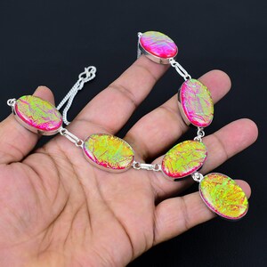 Puede incluir: Un collar plateado con piedras ovaladas iridiscentes en tonos rosa y amarillo-verdoso. Las piedras est&aacute;n unidas por peque&ntilde;os eslabones plateados, creando un accesorio vibrante. El collar se muestra sobre un fondo oscuro. Las piedras miden unos 2 cm.