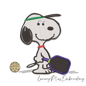 May include: Embroidered image of a cartoon dog playing pickleball. The dog is white with black ears and a black hat, wearing a green headband and a red collar. It holds a purple paddle and a yellow ball.