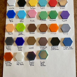 May include: A chart showing different colors of filament for 3D printing. The colors include white, black, yellow, cyan, red, silver, dark blue, light blue, pink, green, peach, brown, copper, orange, gray, purple, wood, silver and copper, black to green with glitter, silver blue with glitter, orange red with glitter, glow in the dark, purple green blue, and purple blue yellow.