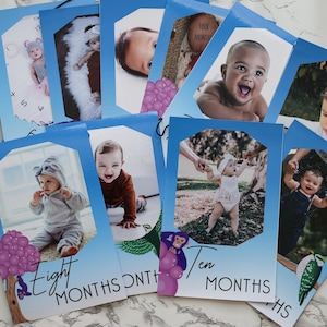 Puede incluir: Un conjunto de tarjetas fotográficas de hitos para bebés con bordes azules. Cada tarjeta presenta una foto diferente del bebé y el mes de su edad. Algunas tarjetas tienen ilustraciones de árboles y animales. Las tarjetas están dispuestas sobre una superficie blanca.