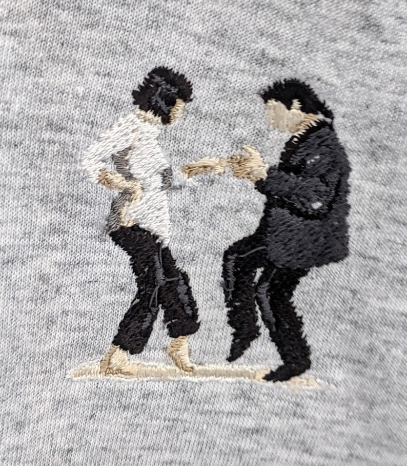 May include: Embroidered image of two figures in black and white, dancing. The figure on the left is wearing a white shirt and black pants, while the figure on the right is wearing a black suit.