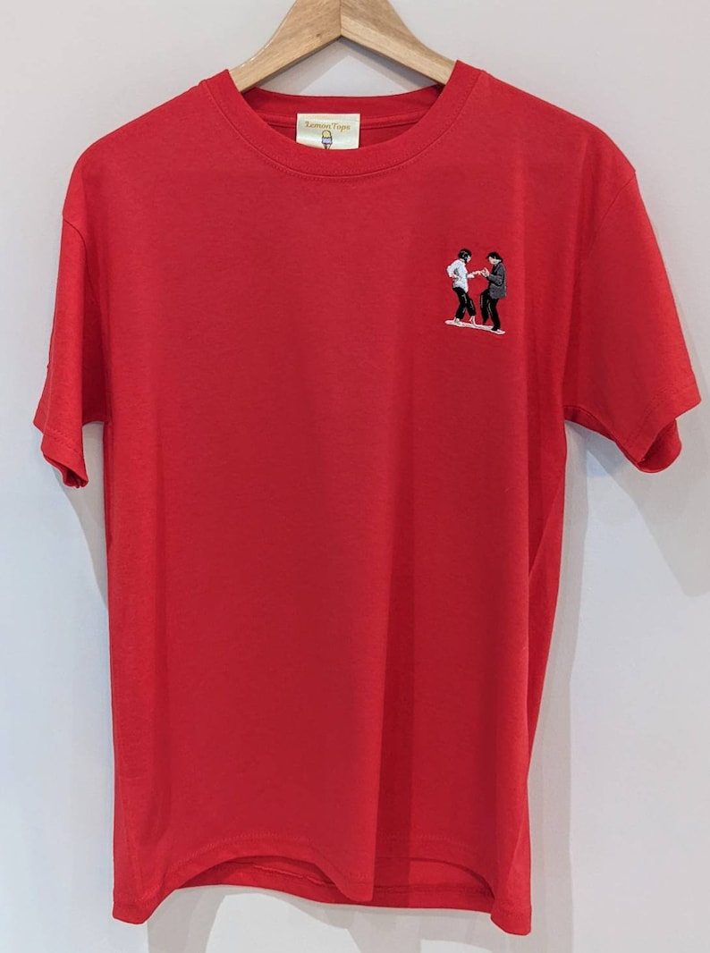 May include: Red short-sleeved t-shirt with an embroidered image of two people dancing. The t-shirt has a small tag on the front that says "Lemon Type".