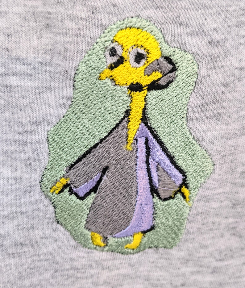 May include: Embroidered patch of a cartoon character with a yellow head, gray body, and purple sleeves. The character is wearing a robe and has a green background.