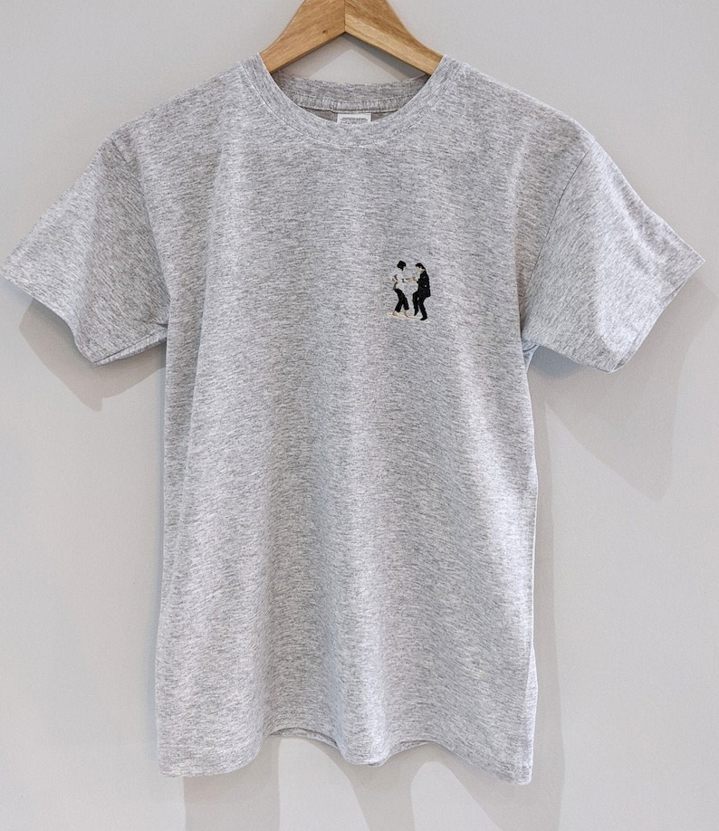May include: A heather gray t-shirt with a small black and white embroidered image of two people dancing.