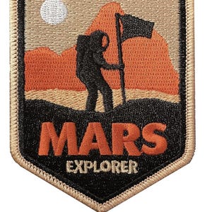Op de afbeelding: Een geborduurde patch met een zwart silhouet van een astronaut die een vlag plant op een rood en oranje bergketen. De tekst "MARS EXPLORER" staat onder de afbeelding in oranje en witte letters op een zwarte achtergrond.