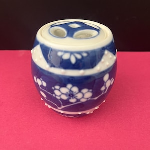 May include: A blue and white ceramic container with a floral design. The container is cylindrical with a rounded top and bottom. The top has two holes. The floral design is white on a blue background.