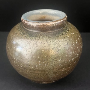 May include: A small, round ceramic vase with a wide, bulbous body and a narrow, circular opening. The exterior features a mottled, earthy glaze in shades of olive green, brown, and tan, with a smooth, glossy finish and subtle white speckling.