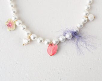 May include: A white pearl necklace with a pink flower charm, a pink heart charm, and a purple feather charm.