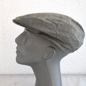 Puede incluir: Una gorra de newsboy de cuadros grises y marrones con una visera ligeramente curvada.