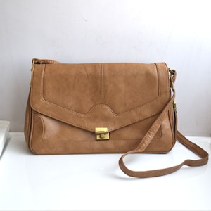 Peut inclure: Un sac à bandoulière en cuir marron avec une fermeture à rabat et un fermoir doré. Le sac a une longue bandoulière réglable.