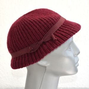 Puede incluir: Un gorro de punto burdeos con un ala ancha y una cinta burdeos a juego atada en un lazo en la parte delantera.