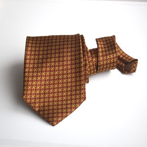 May include: A red and gold patterned silk tie. The tie has a geometric pattern of squares and circles.