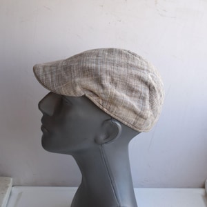 May include: A beige and brown checked newsboy cap. The cap is made of a woven material and has a rounded crown and a short, rigid peak. The cap is shown on a mannequin head.