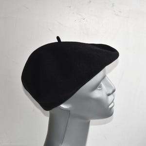 May include: A black beret hat, a classic style of headwear. The beret is made of a soft, textured material and features a small, rounded top. This hat is a versatile accessory, suitable for various occasions.