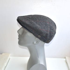 May include: A gray tweed newsboy cap with a black leather band and a red and white plaid pattern.