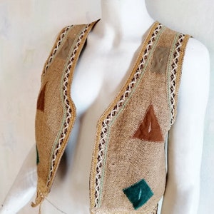 May include: A brown sleeveless vest with a geometric pattern of triangles and squares. The vest is made of a woven fabric and has a fringed edge.