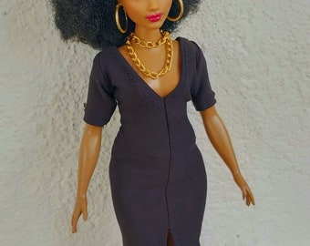 Può includere: Una bambola nera con un'acconciatura afro che indossa un vestito nero, orecchini a cerchio dorati e una collana a catena dorata. La bambola indossa sandali marroni.