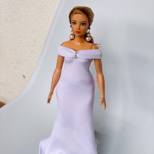 May include: A white off-the-shoulder gown with a fitted bodice and a flowing skirt. The doll is wearing pearl earrings.