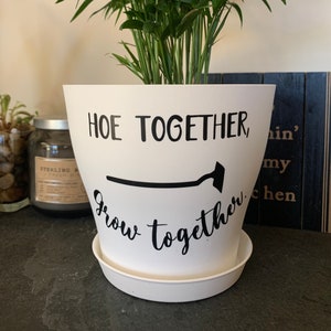 May include: White ceramic plant pot with black text that reads "Hoe Together, Grow Together" and a black silhouette of a garden hoe.