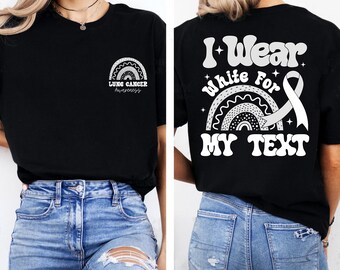 Puede incluir: Camiseta negra con un diseño de arcoíris y el texto "LUNG CANCER Awareness" en la parte delantera. La parte trasera de la camiseta presenta el texto "I Wear White For MY TEXT" con una cinta blanca y un gráfico de arcoíris.