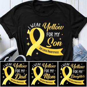 以下が含まれることがあります： 黄色いリボンと「I Wear Yellow For My Son Sarcoma Awareness」の文字が入った黒いTシャツ。「Dad」、「Mom」、「Daughter」のバリエーションも。デザインには蝶と星が描かれています。