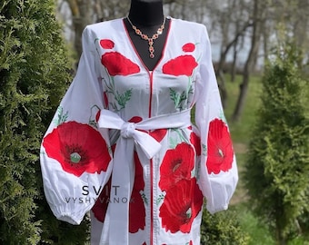 May include: White dress with red poppy floral embroidery. The dress features long sleeves, a V-neck, and a matching belt. The text "SVIT VYSHYVANOK" is visible on the lower left side of the dress. A necklace is worn on the mannequin.