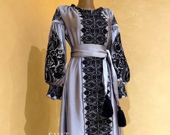 May include: A long, light blue satin dress with black embroidered floral patterns. The dress has a sash tied at the waist and features a tassel at the bottom.