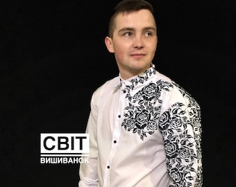 Könnte beinhalten: Ein weißes Langarmhemd mit schwarzen gestickten Blumendesigns auf der Vorderseite und den Ärmeln. Das Hemd hat einen Knopfkrag und schwarze Knöpfe. Der Text "СВІТ ВИШИВАНОК" ist auf dem Hemd sichtbar.