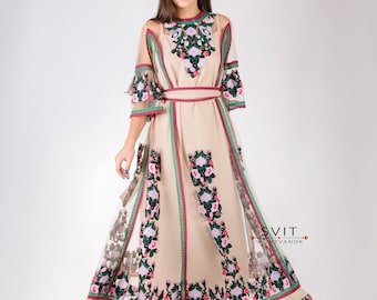 May include: A beige embroidered dress with floral patterns in pink, green, and purple. The dress has a sheer overlay and a red belt. The dress is made by SVIT VYSHIVANOK.