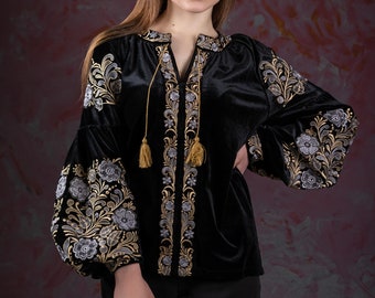 May include: A black velvet blouse with gold and silver embroidery. The blouse has a V-neck and long sleeves with a gathered cuff.