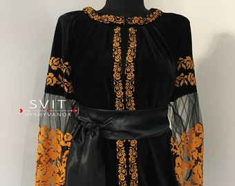 May include: Black velvet blouse with long sleeves and a black satin sash. The sleeves are sheer and feature a gold embroidered floral pattern. The blouse has a round neckline and a gold embroidered floral pattern around the neckline.