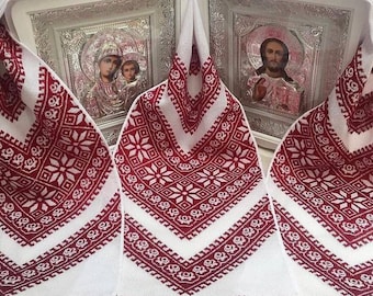 Könnte beinhalten: Zwei gerahmte religiöse Ikonen mit silbernen Rahmen und Glasfronten, bedeckt mit einem weißen bestickten Tuch mit roten und weißen geometrischen Mustern.