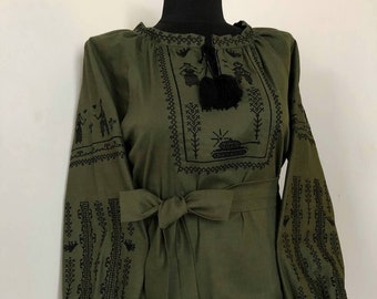 May include: A green embroidered blouse with black embroidery featuring a tank and trees. The blouse has a tie at the waist and the text "SVIT VYSYVANO"