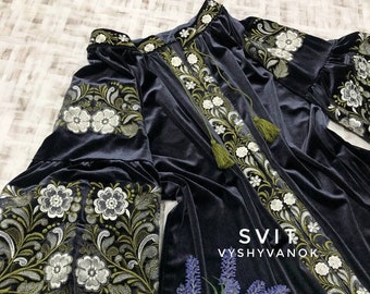 May include: A dark blue velvet dress with white and green embroidered floral patterns. The dress has long sleeves and a round neckline. The text "SVIT VYSYVANOX" is embroidered on the dress.