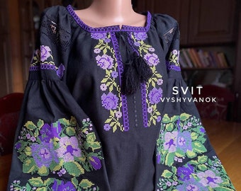 May include: Black embroidered blouse with a floral design in shades of purple, green, and yellow. The blouse has a tassel tie at the neckline and long sleeves. The text "SVIT VYSHYVANOK" is visible on the bottom right corner of the image.