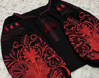 May include: Black embroidered blouse with red and purple floral designs. The blouse has a gathered neckline and long sleeves with embroidered cuffs. The text "SVIT VYS SHYVANOK" is visible on the bottom of the blouse.