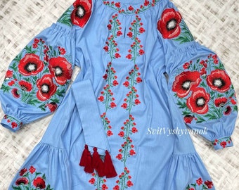 May include: A light blue embroidered dress with red poppy flowers and green stems. The dress has a round neckline and long sleeves. The dress has a sash with red tassels.