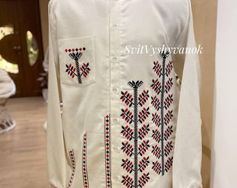 May include: Cream-colored long-sleeve shirt with intricate black and red embroidered patterns. Features a mandarin collar, button-down front, and a pocket on the left chest. The text "SvitVyshyvanok" is visible on the right side. The cuffs and hemline are also detailed with embroidery.