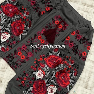 A gray long-sleeved blouse featuring vibrant red, white, and black floral embroidery on the chest and sleeves, with a dark red drawstring tassel at the neckline.
