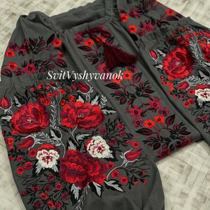 A close-up shot of a dark gray embroidered blouse highlighting the detailed red and white floral patterns along the sleeve and neckline.