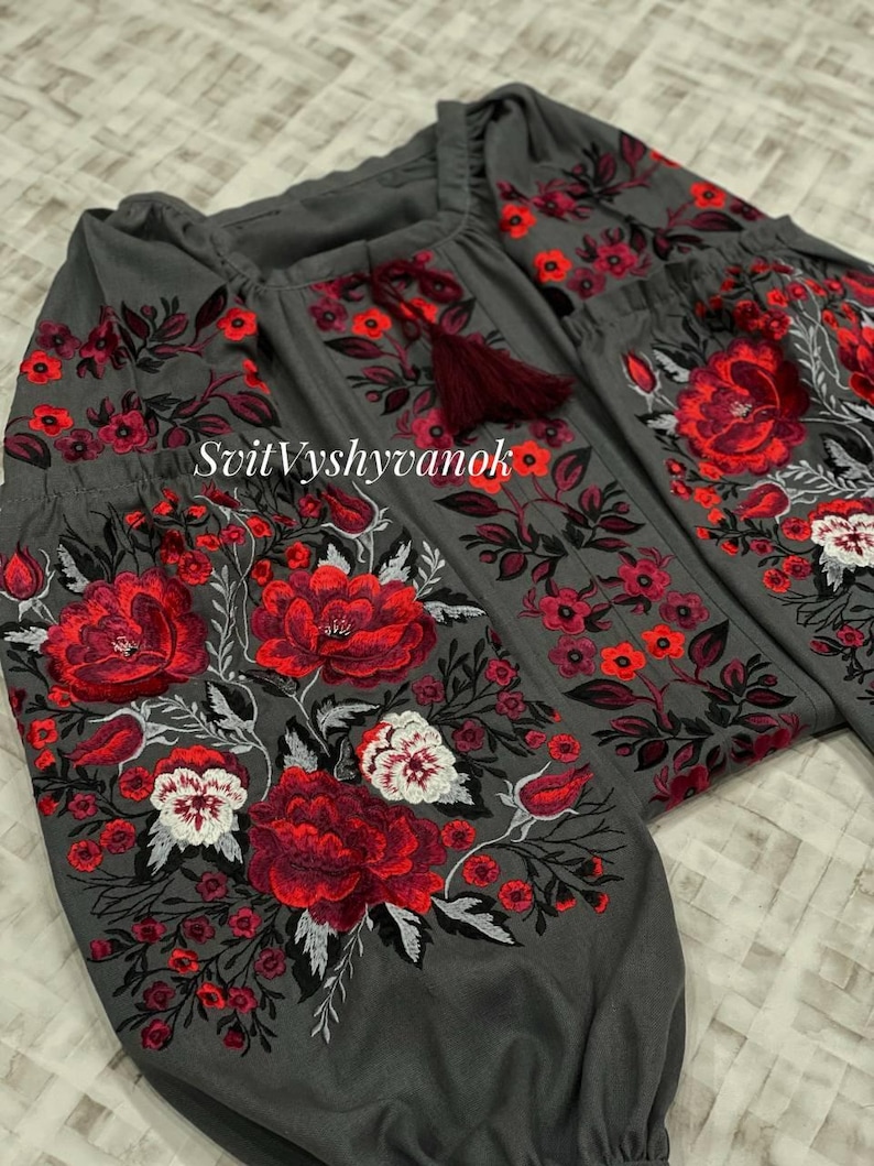 A close-up shot of a dark gray embroidered blouse highlighting the detailed red and white floral patterns along the sleeve and neckline.