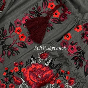 A detailed close-up view of the red and white floral embroidery and dark red tassel on a gray fabric garment.