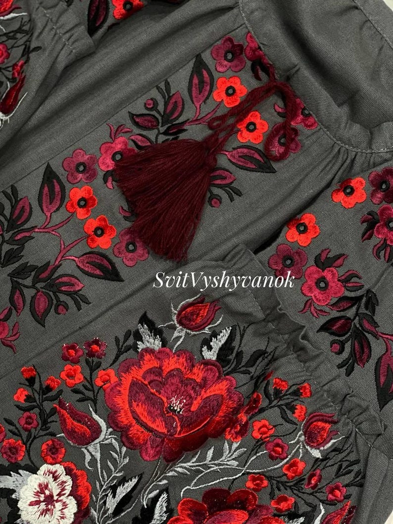A detailed close-up view of the red and white floral embroidery and dark red tassel on a gray fabric garment.