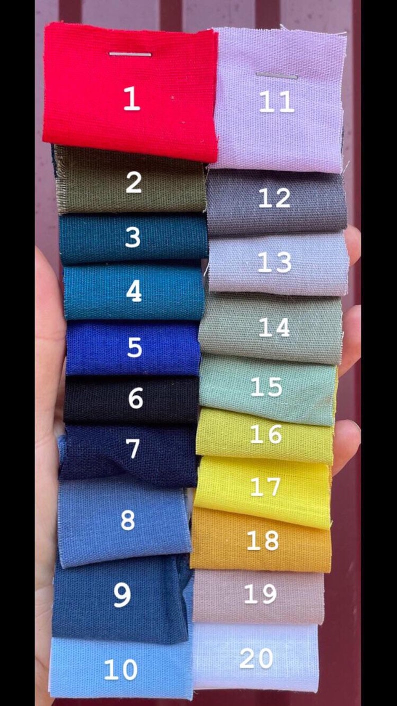 A hand holding twenty small fabric color swatches numbered one through twenty in two columns, showing various shades of red, green, blue, yellow, purple, and neutral tones.