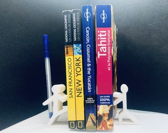 May include: A white bookend shaped like two people holding up four travel guide books. The books are titled "San Francisco", "New York", "Cancun, Cozumel & the Yucatan", and "Tahiti et la Polynesie Francaise".