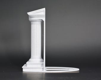 Może przedstawiać: Biała podpórka do książek o klasycznym architektonicznym wzorze kolumny z pionowymi żłobieniami, kwadratową podstawą i trójkątnym frontonem. Konstrukcja zawiera płaską, wydłużoną poziomą płytę wsporczą wychodzącą z podstawy.